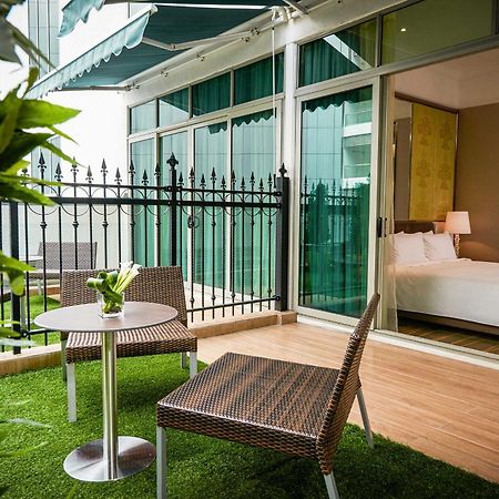 Dorsett Putrajaya Hotel Exterior photo The photo shows a small outdoor balcony or terrace area featuring two wicker-style chairs and a round table. The floor is covered with artificial grass, creating a cozy and inviting atmosphere. In the background, there is a glass wall that leads into