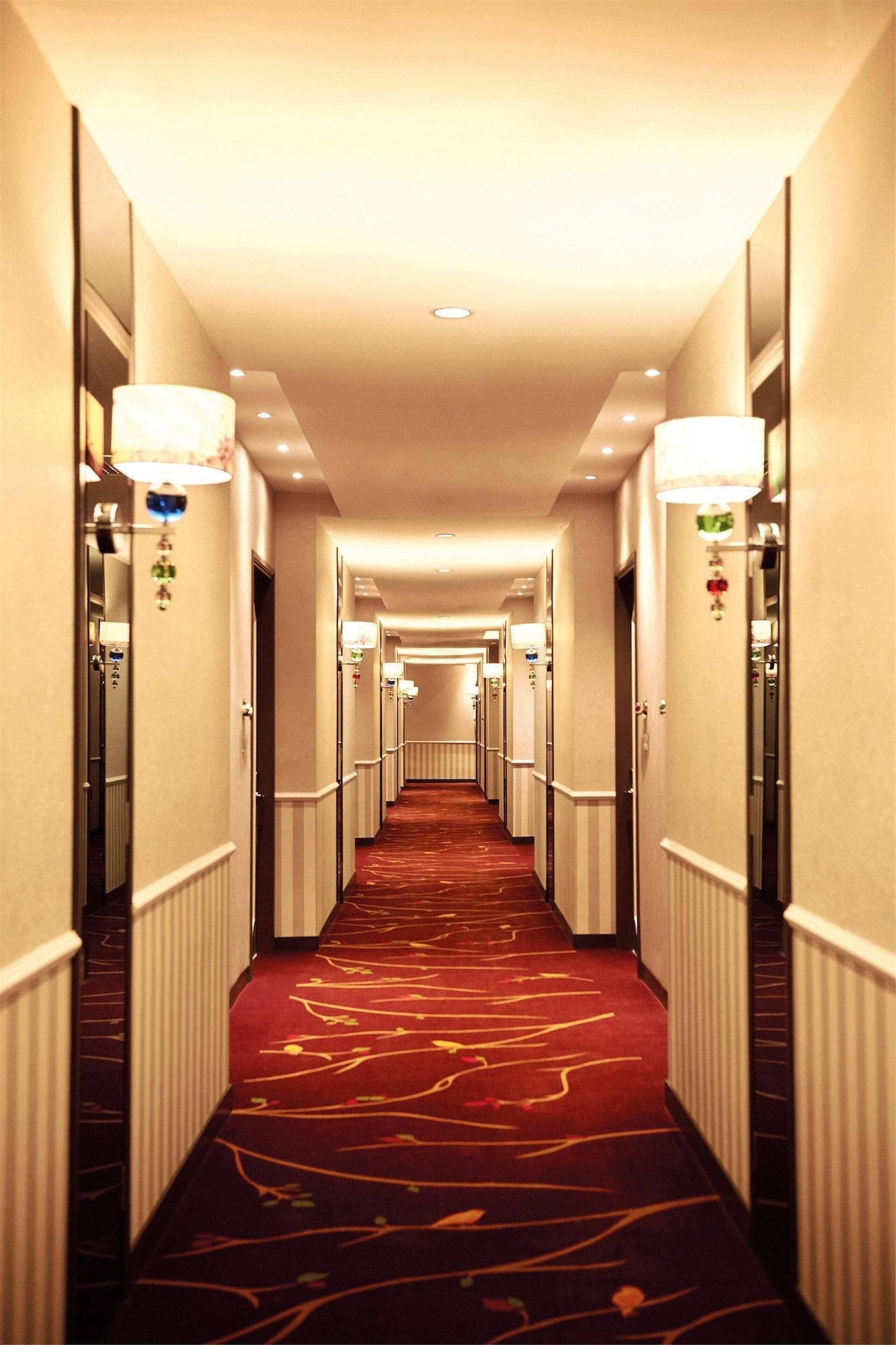 Dorsett Putrajaya Hotel Exterior photo The photo shows a hotel corridor with a long perspective. The walls are painted in a light color, and the floor is covered with a red carpet featuring stylized patterns. There are several closed doors along both sides of the hallway, likely leading t