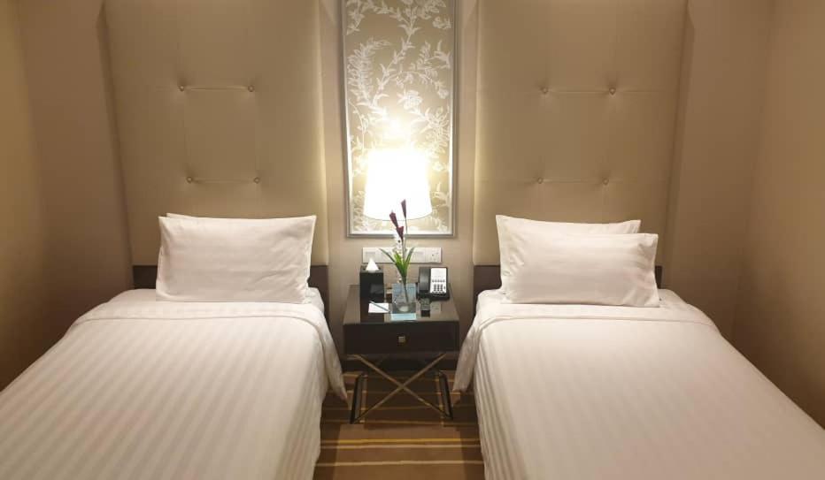 Dorsett Putrajaya Hotel Exterior photo The photo shows a cozy hotel room featuring two twin beds with white bedding. Each bed has a neatly arranged white pillow. Between the beds is a small bedside table, which holds a lamp, a couple of decorative plants, and some electronic devices. The 