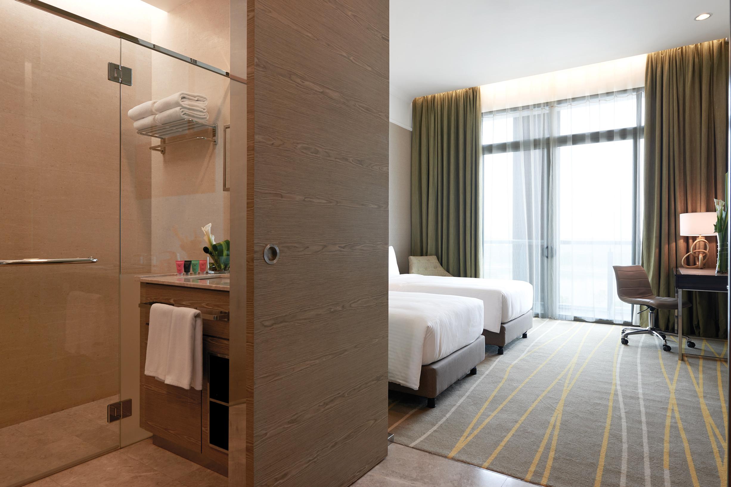 Dorsett Putrajaya Hotel Exterior photo The photo shows a modern hotel room with a clean and inviting design. On the left side, there is a bathroom area featuring a glass shower and some neatly arranged towels. The bathroom has a sink with toiletries and a small shelf. 

On the right side,