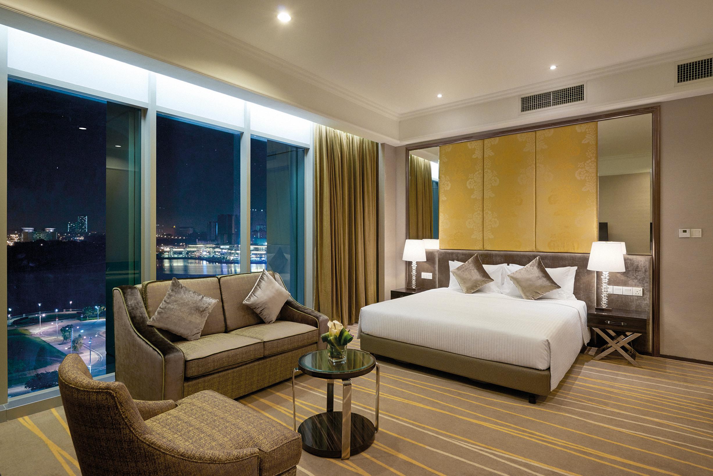 Dorsett Putrajaya Hotel Exterior photo The photo shows a hotel room designed for comfort and modern aesthetics. It features a large bed with crisp white linens, accompanied by decorative pillows. To one side, there is a cozy seating area with a sofa and an armchair, positioned around a sm