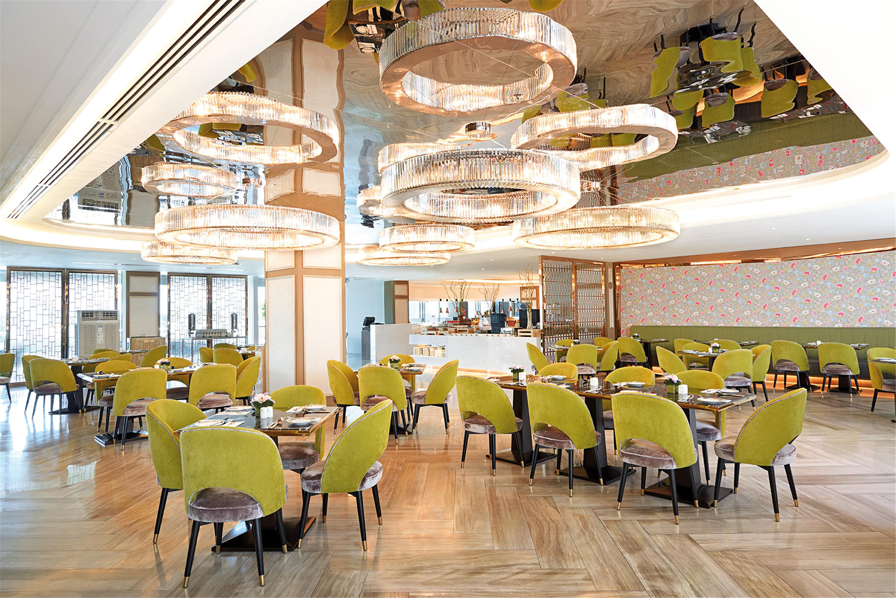 Dorsett Putrajaya Hotel Exterior photo The photo shows a modern dining area with stylish décor. There are several round tables arranged throughout the space, each accompanied by vibrant green chairs. The ceiling features large, circular light fixtures that create an eye-catching design. T