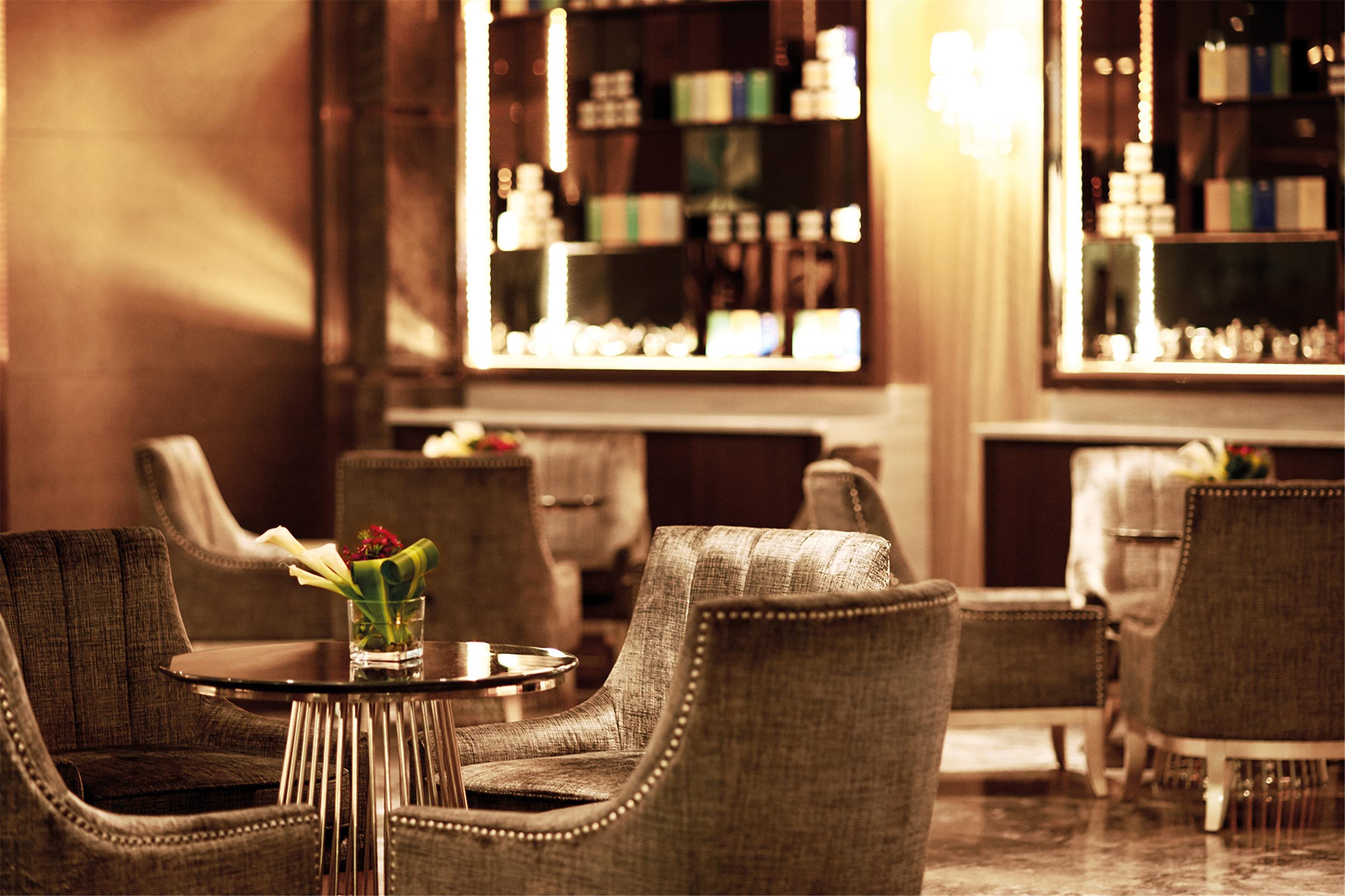 Dorsett Putrajaya Hotel Exterior photo The image depicts a stylish and elegant interior of a lounge or seating area. It features plush, modern armchairs arranged around a small table. The chairs have a textured fabric and are adorned with decorative nailhead trim. On the table, there is a