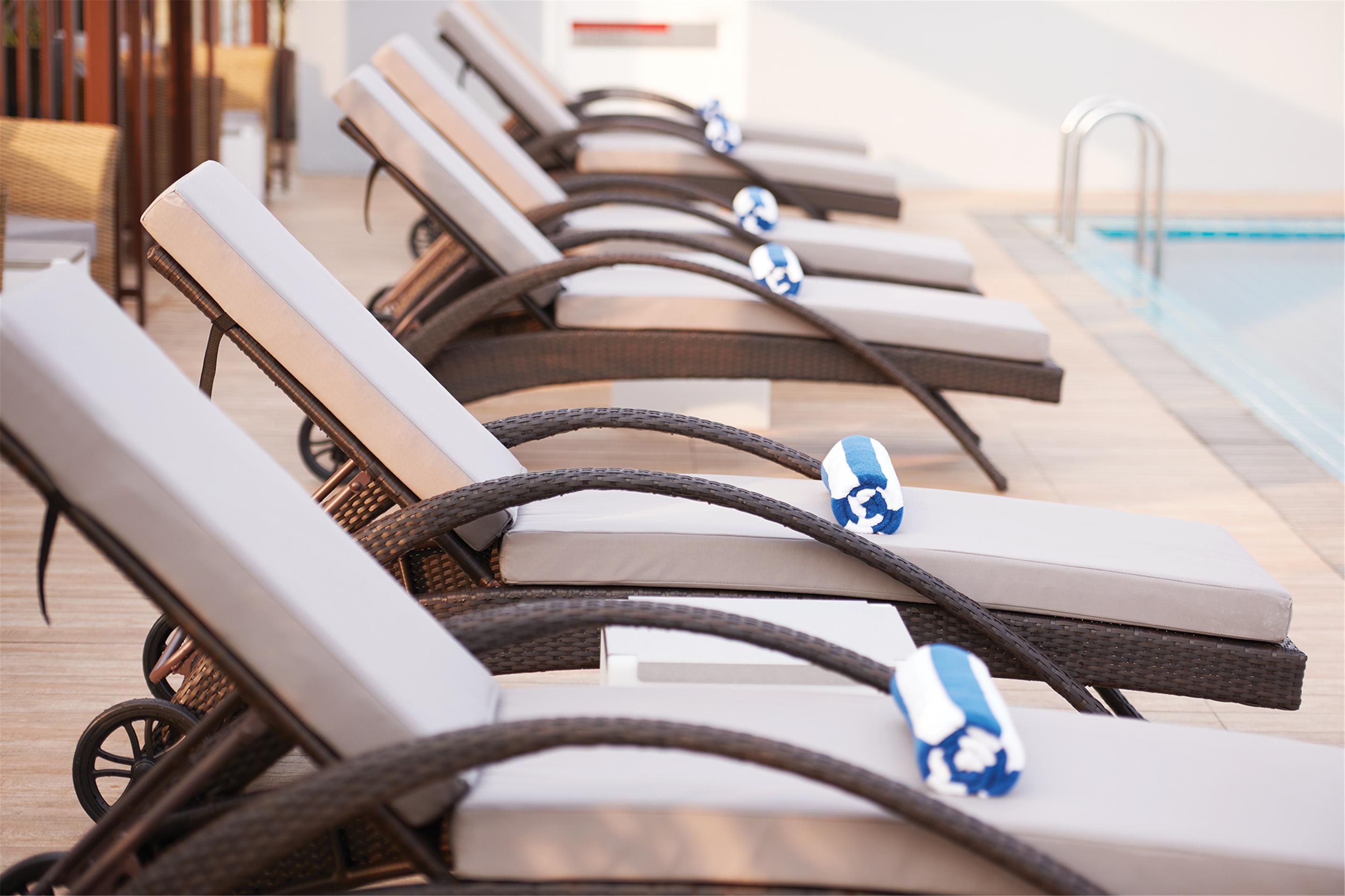 Dorsett Putrajaya Hotel Exterior photo The photo shows a row of reclined lounge chairs that are lined up next to a swimming pool. Each chair has a light-colored cushion and is accompanied by a blue and white rolled towel placed on the seat. The setting appears to be a sunny, relaxing area