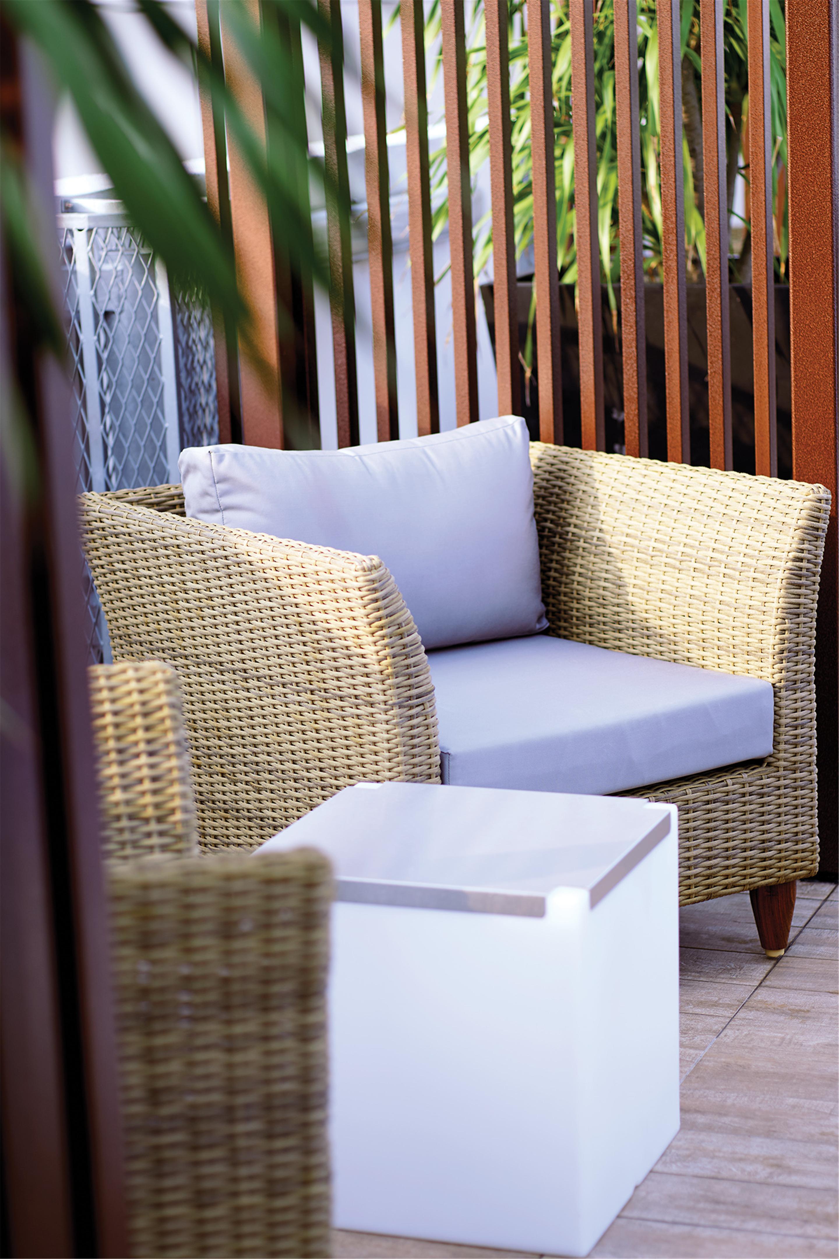 Dorsett Putrajaya Hotel Exterior photo The photo shows a cozy seating area featuring a wicker chair with a light cushion placed on the seat. The chair is part of a patio or outdoor setting, and there is a small, white side table next to it. The background includes wooden slats, suggesting