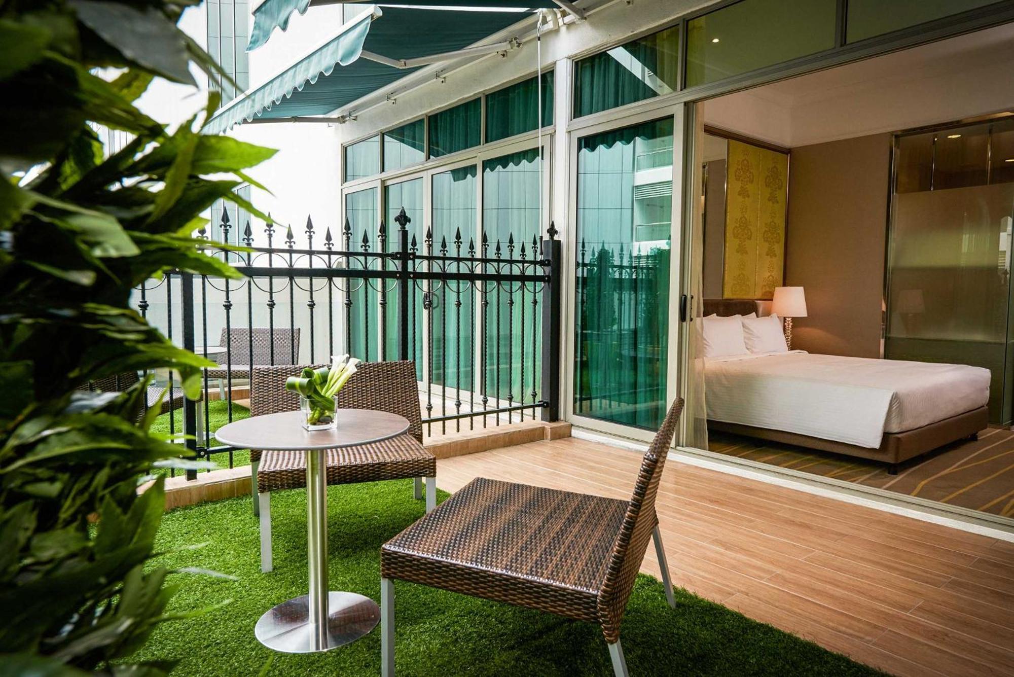 Dorsett Putrajaya Hotel Exterior photo The photo shows a small outdoor balcony or terrace area featuring two wicker-style chairs and a round table. The floor is covered with artificial grass, creating a cozy and inviting atmosphere. In the background, there is a glass wall that leads into