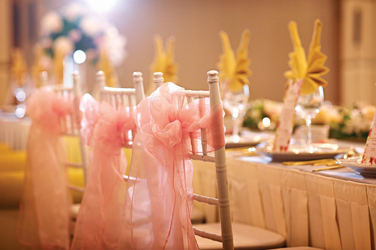Dorsett Putrajaya Hotel Exterior photo The photo depicts a beautifully arranged dining setup, likely for a special event like a wedding or celebration. Wooden chairs, adorned with soft pink sashes, are lined up, creating an elegant atmosphere. The table is set with white tablecloths and f