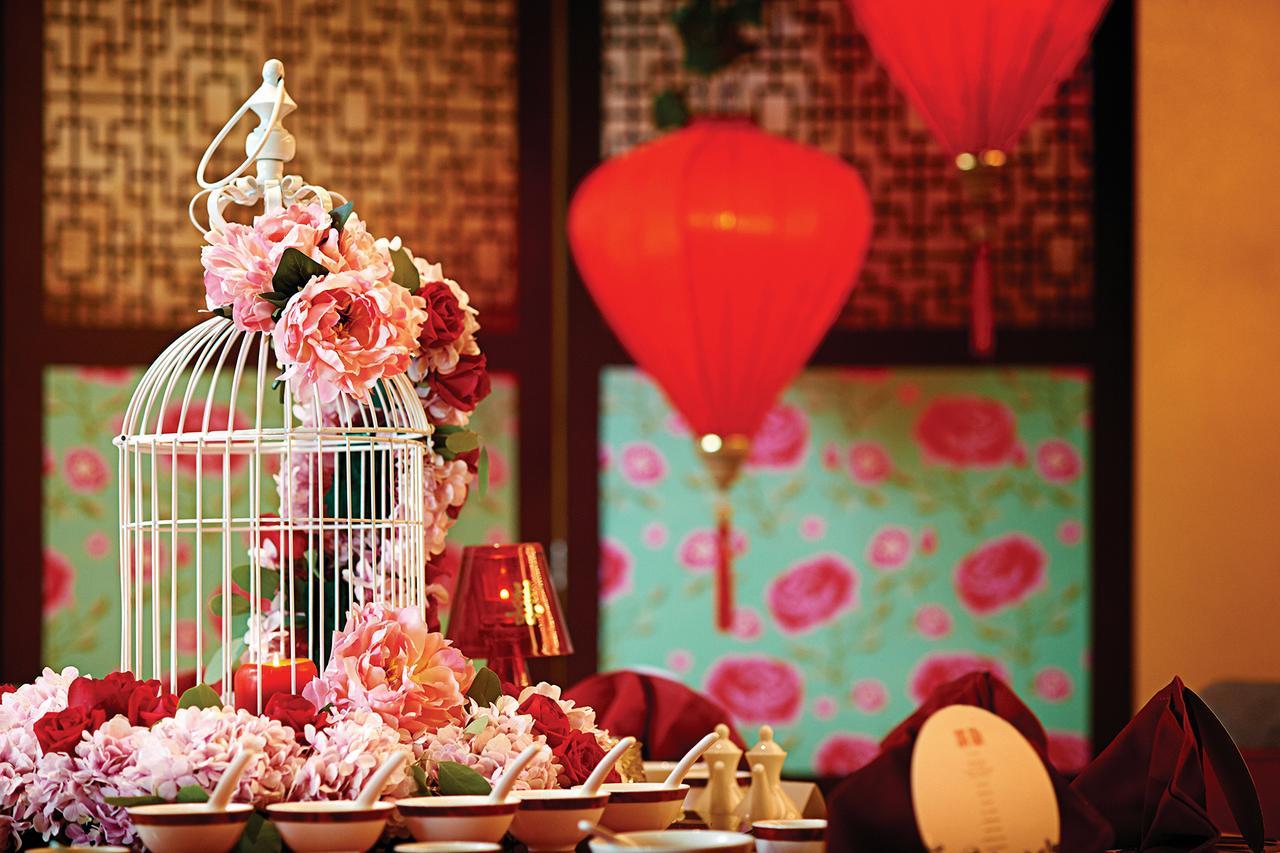 Dorsett Putrajaya Hotel Exterior photo The photo shows a beautifully decorated table setting with an elaborate centerpiece. The centerpiece features a white birdcage adorned with pink and red flowers. Surrounding the birdcage are additional floral arrangements that complement the colors. 