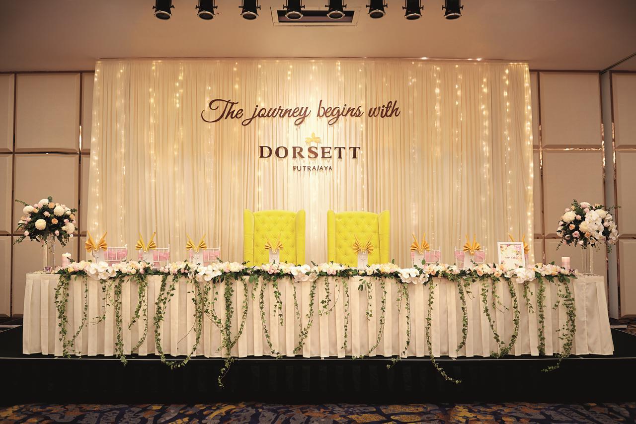 Dorsett Putrajaya Hotel Exterior photo The photo depicts a decorated event space, likely set up for a celebration or ceremony. In the center, there is a backdrop with the phrase "The journey begins with DORSETT" prominently displayed. The backdrop is adorned with elegant draping and soft 