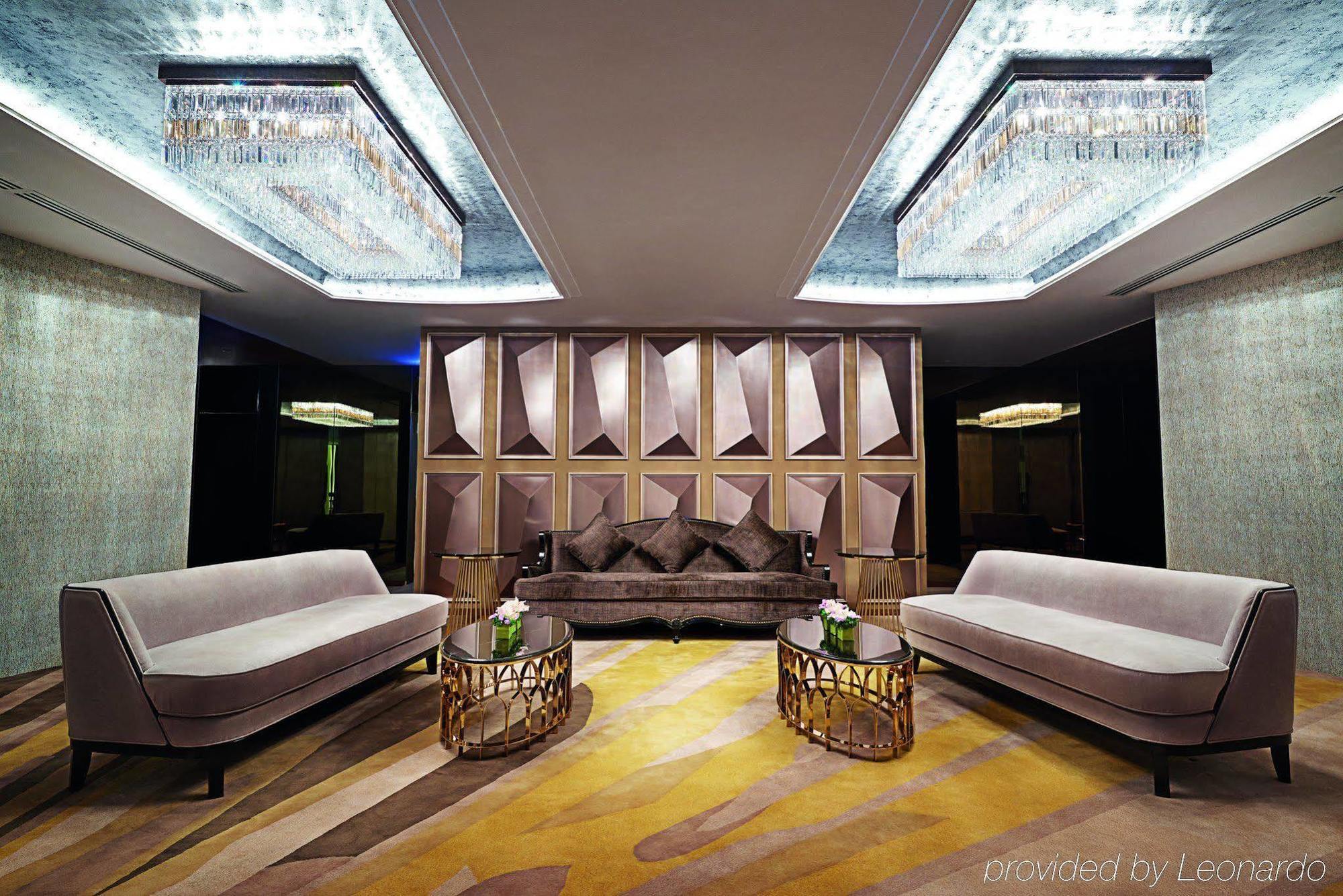 Dorsett Putrajaya Hotel Exterior photo The photo shows an elegantly designed modern living space or lounge area. It features two plush, light-colored sofas facing a central dark-colored sofa adorned with decorative pillows. The walls have a geometric design with a luxurious finish, and th