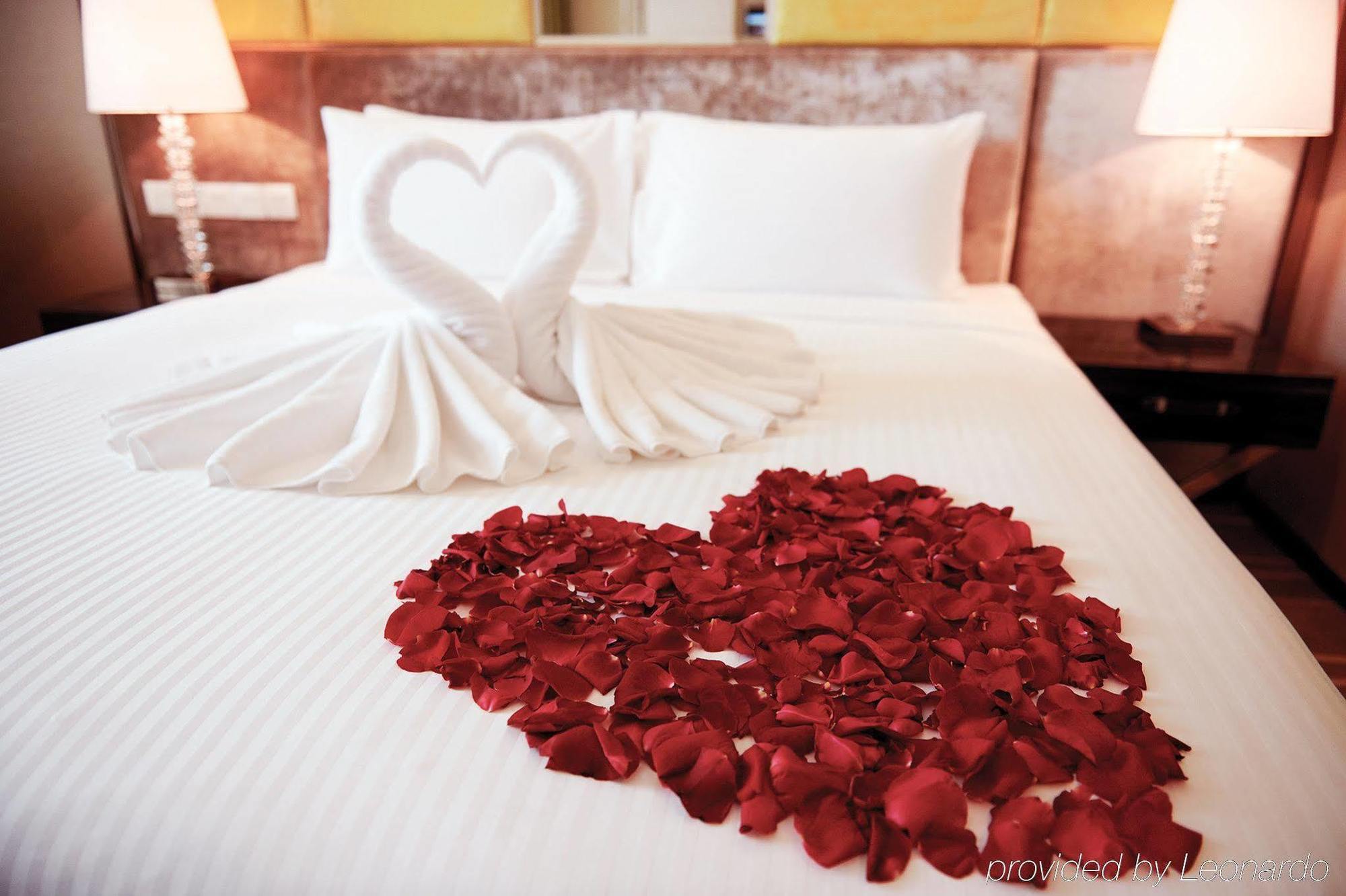 Dorsett Putrajaya Hotel Exterior photo The photo shows a beautifully arranged bed with white bedding. On the bed, there is a decorative figure made from towels shaped like two swans forming a heart. Surrounding this figure is a heart made of red rose petals, adding a romantic touch to the