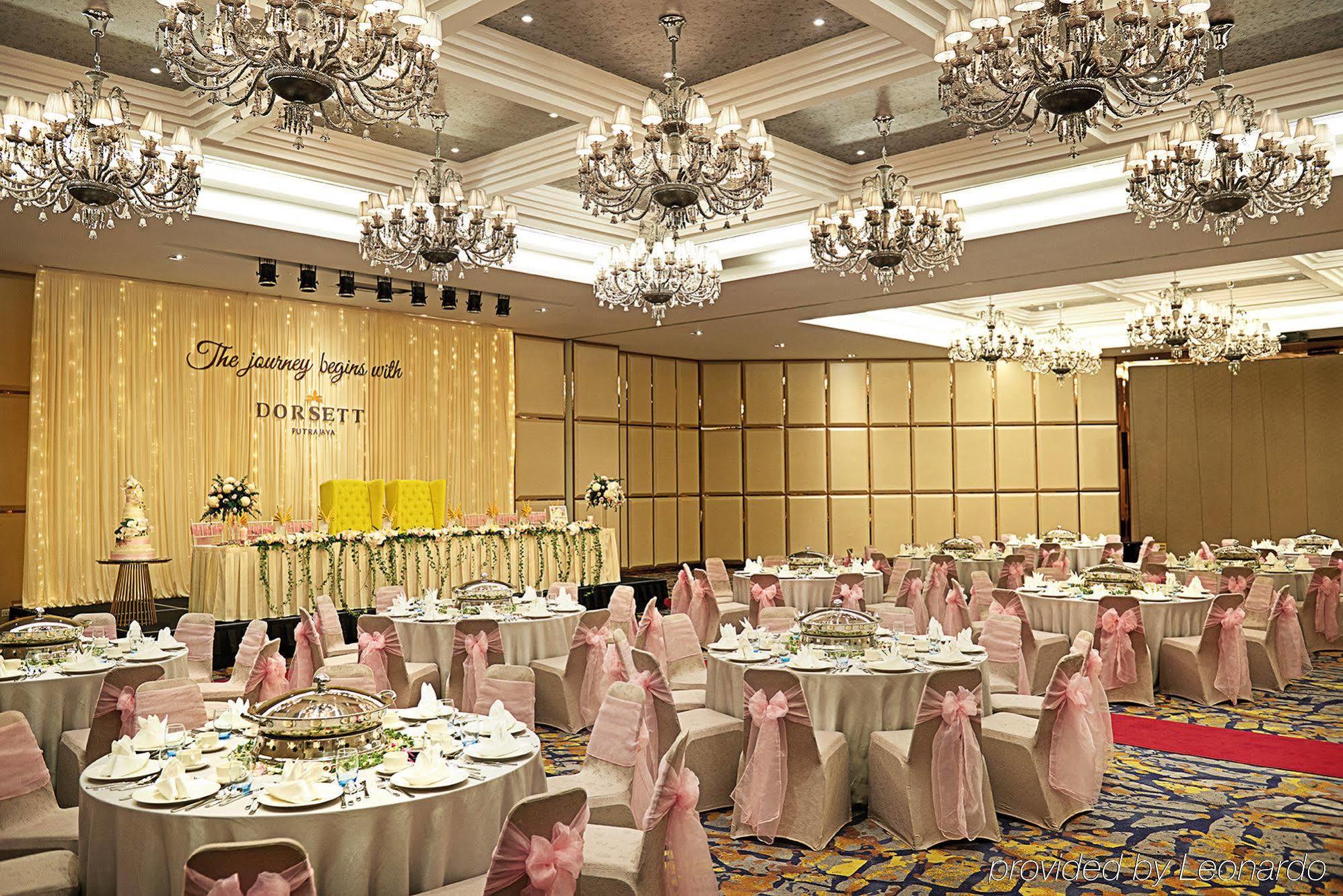 Dorsett Putrajaya Hotel Exterior photo The photo shows an elegant banquet hall set up for a celebration or event. The room features numerous round tables covered with white tablecloths and adorned with pink sashes on the chairs. There are decorative centerpieces on the tables, and the wal