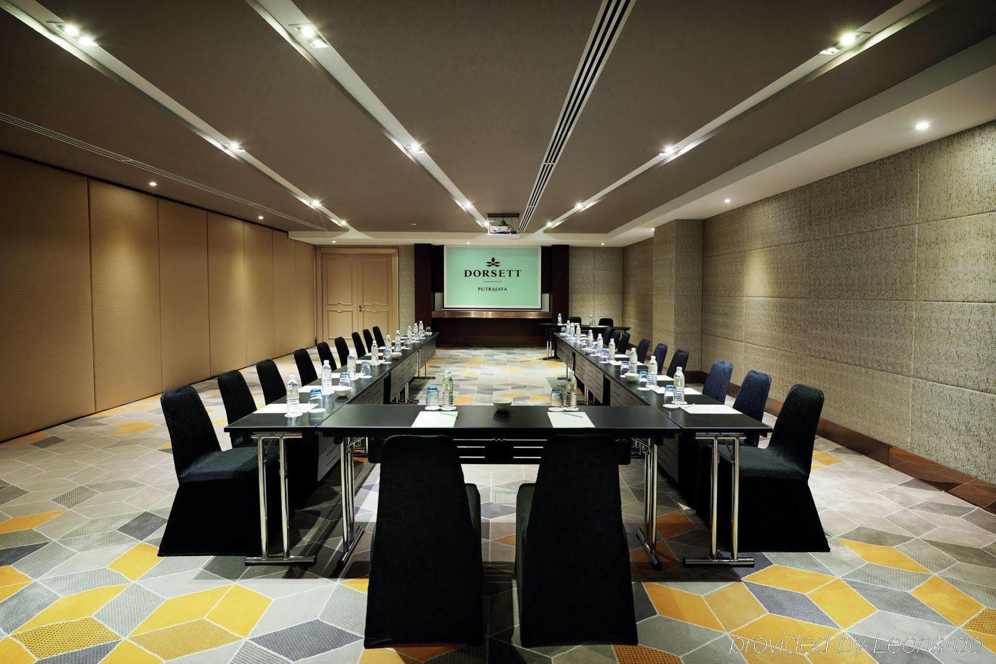 Dorsett Putrajaya Hotel Exterior photo The photo shows a modern conference room arranged for a meeting. In the center, there is a large rectangular table surrounded by sleek black chairs. At the front of the room, there's a presentation screen with the name or logo displayed. The walls ar