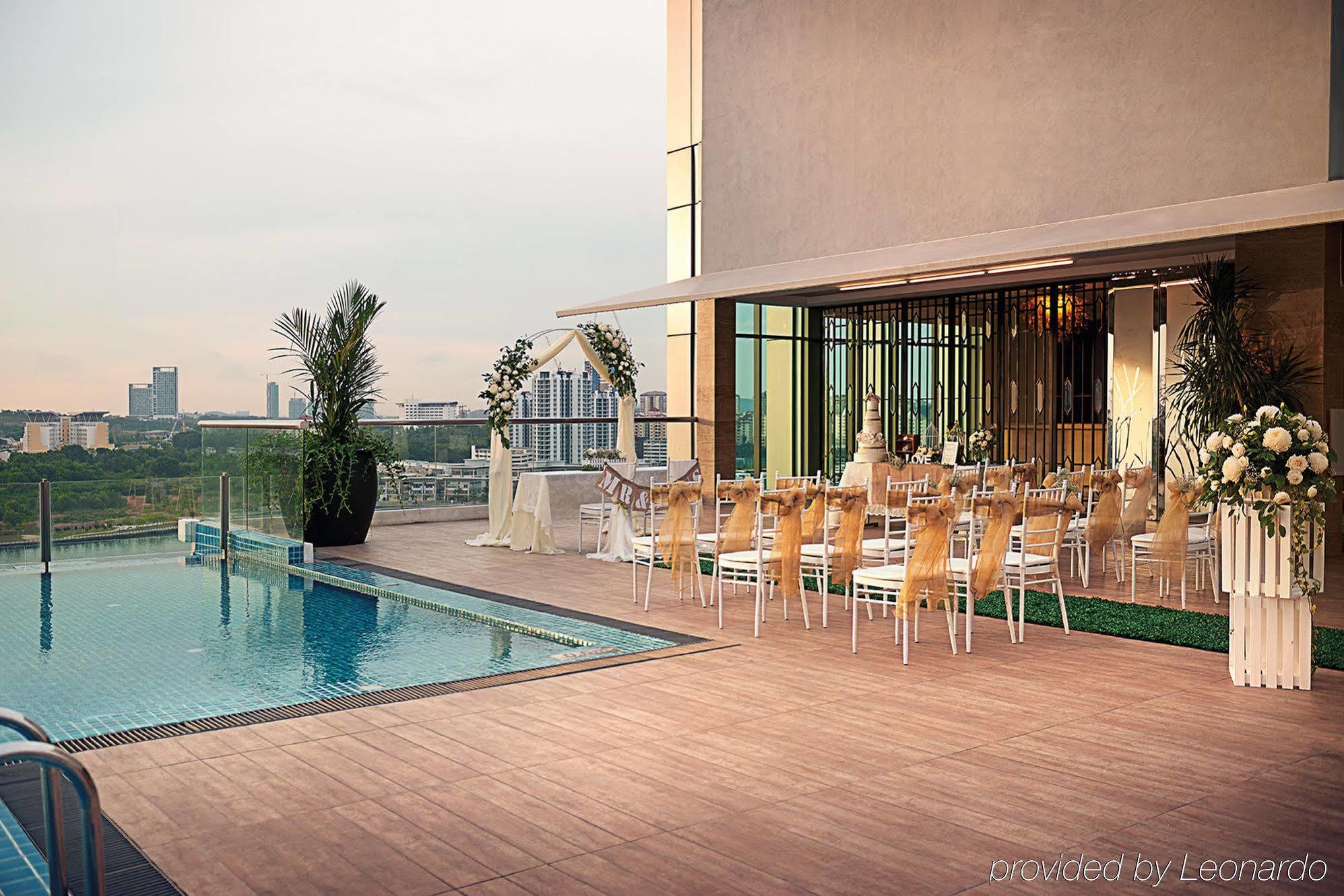 Dorsett Putrajaya Hotel Exterior photo The photo shows an outdoor area featuring a swimming pool adjacent to a spacious terrace. On the terrace, there are several elegantly arranged tables and chairs, suggesting it is set up for an event, possibly a wedding or a formal gathering. The back