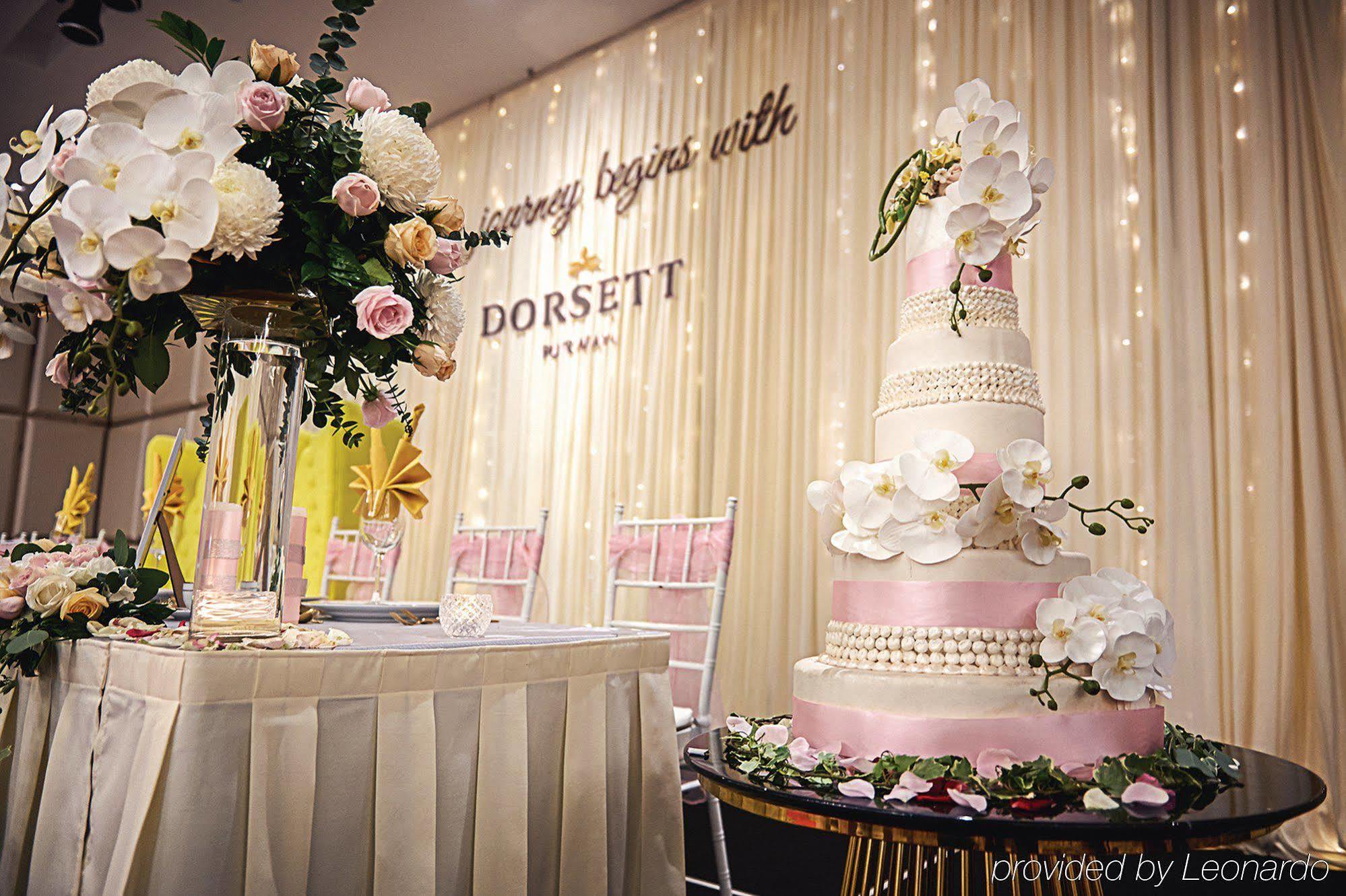 Dorsett Putrajaya Hotel Exterior photo The photo shows a beautifully decorated event space, likely for a wedding or special celebration. On the left, there is a tall floral arrangement featuring white orchids and pink roses, placed on a glass pedestal. The arrangement adds an elegant touc