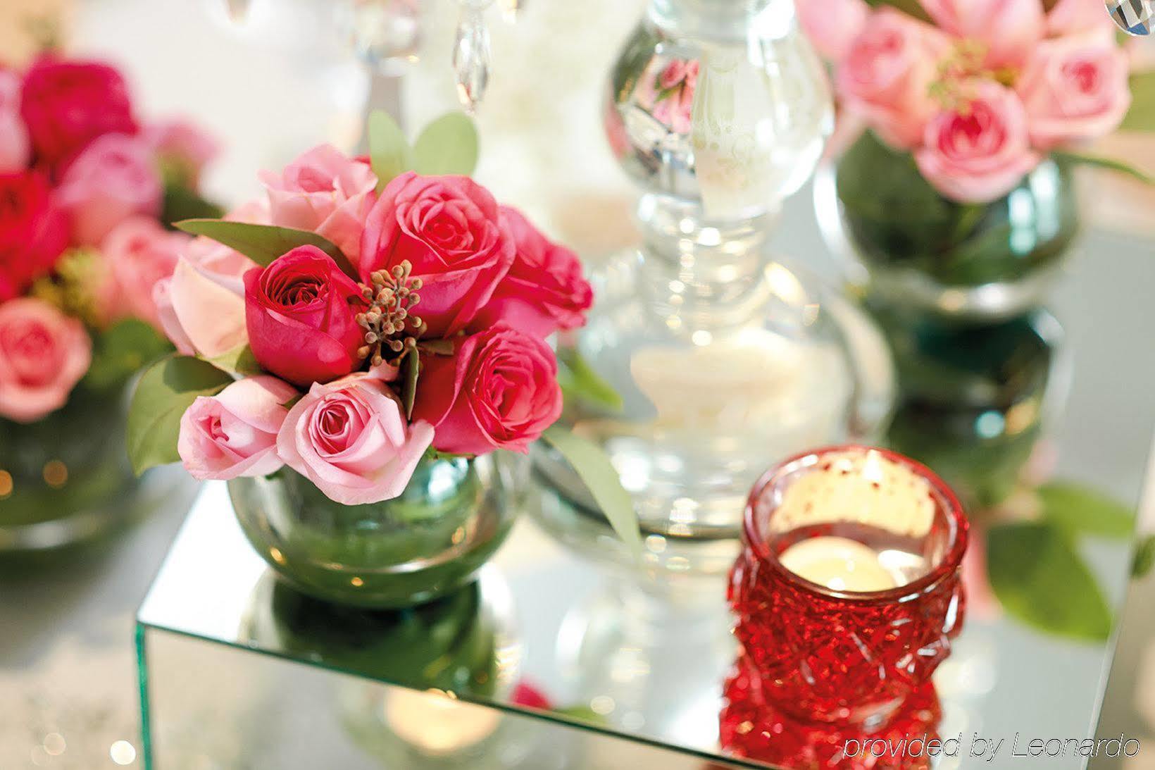Dorsett Putrajaya Hotel Exterior photo The photo features a decorative arrangement of flowers. There are mixed pink roses in a small glass vase, alongside a few green leaves for contrast. The flowers are arranged attractively, and there are additional floral arrangements in the background