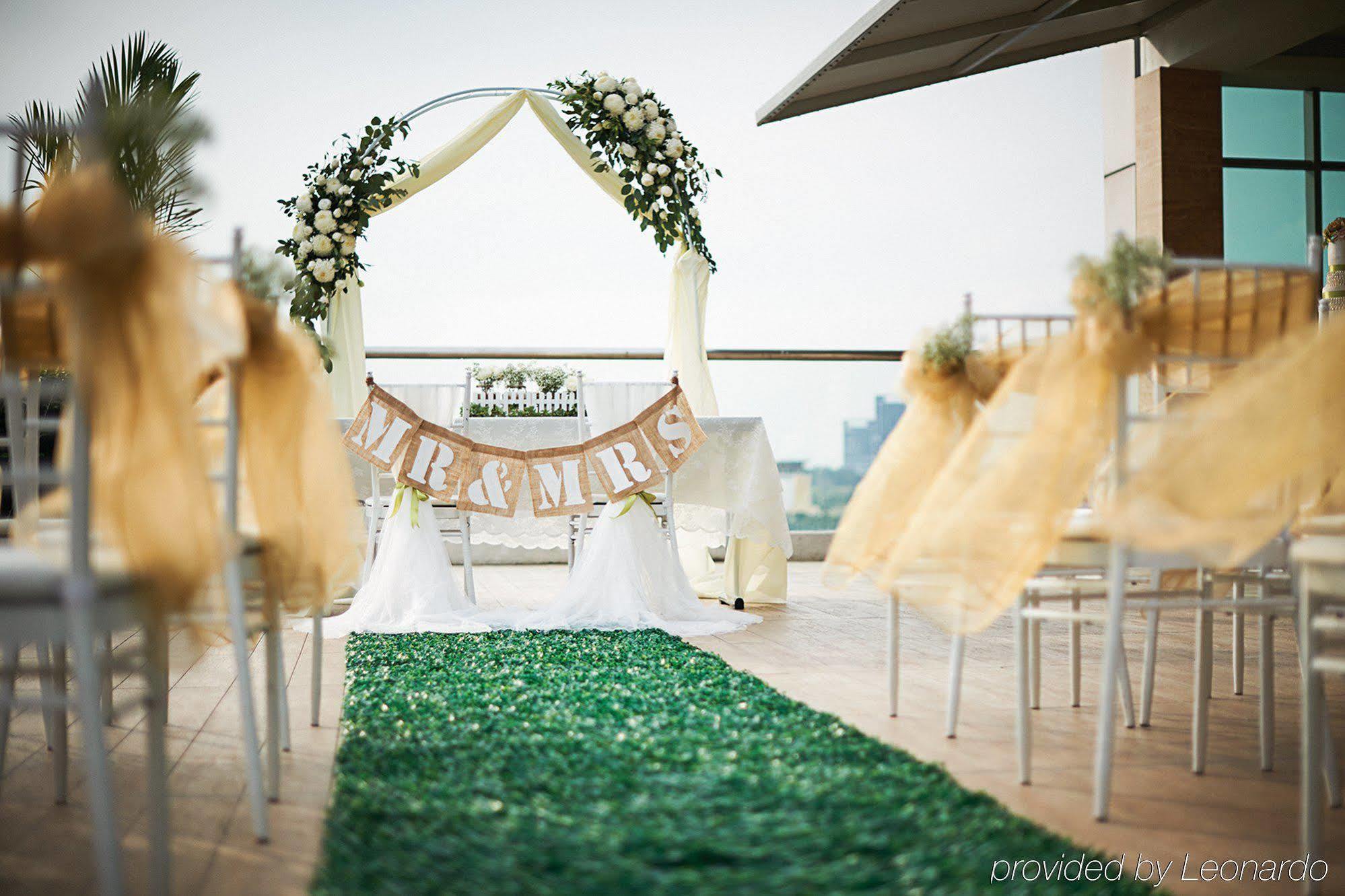 Dorsett Putrajaya Hotel Exterior photo The photo depicts a beautifully arranged outdoor wedding setting. In the foreground, there is a green carpet leading to an altar or archway adorned with flowers and draped fabric. Above the altar, a banner reads "MR & MRS," indicating it is a wedding