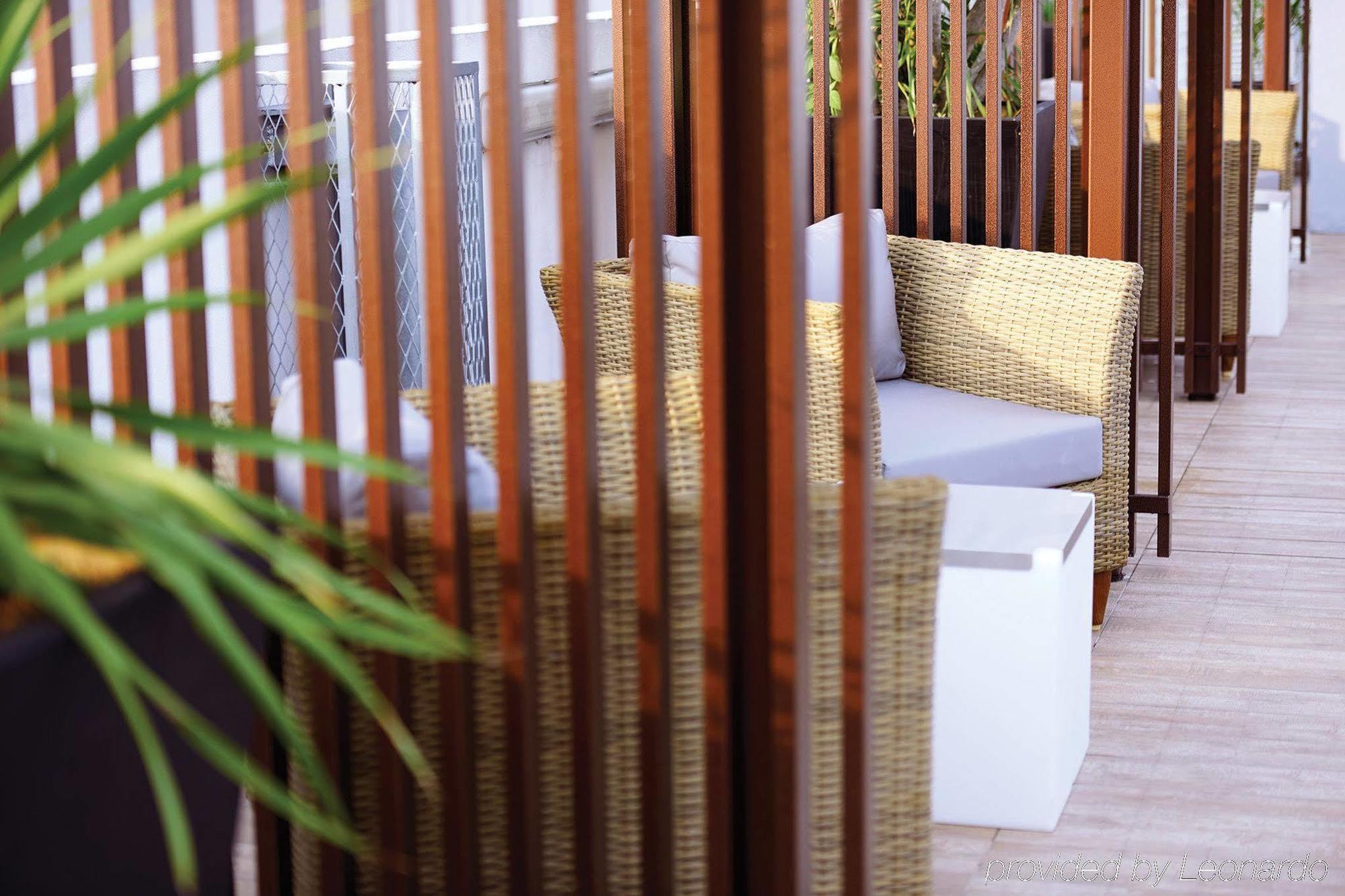 Dorsett Putrajaya Hotel Exterior photo The photo shows a cozy outdoor seating area. There are two wicker chairs with gray cushions positioned near a small white table. The seating is partially surrounded by wooden slats, which create a sense of privacy and separation from the rest of the 